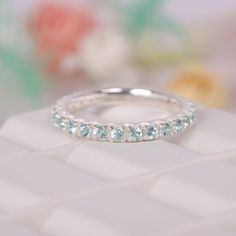 a white gold wedding band with blue topazte stones on the side, and flowers in the background