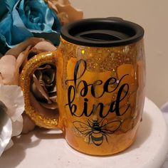 there is a coffee mug with the words bee kind on it next to some flowers