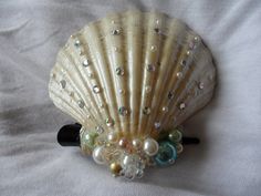 a seashell with pearls and glass beads on it's side sitting on a white sheet