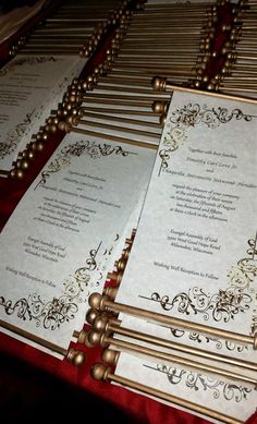 wedding programs are lined up on a red tablecloth with gold trimmings and scrolls