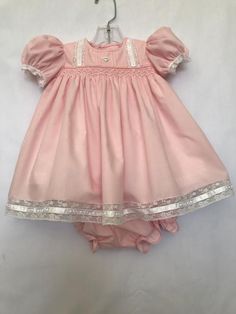 This size 3 mo. dress is made of pink, poly/cotton fabric. Lace insertions and edgings are on the bodice, sleeves and dress bottom. The dress is lined with white polyester cooton. A white heart button is added to the bodice and the back is also fastened with 2 heart buttons. The body of the dress Cotton Baptism Dress With Lining, Fitted Pink Cotton Dress, Cute Pink Lined Dress, Fitted Pink Dress With Buttons, Pink Short Sleeve Baptism Dress, Pink Short Sleeve Dress For Baptism, Cute Pink Dresses With Buttons, Cute Pink Dress With Buttons, Fitted Summer Dresses With Picot Trim