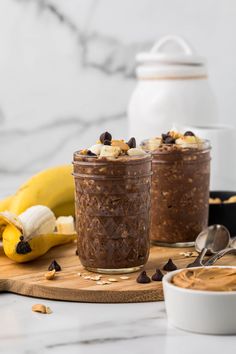 two jars of chocolate chia pudding on a cutting board with bananas and spoons