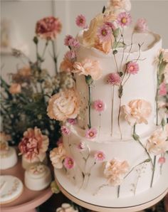 a three tiered cake with flowers on it's side, surrounded by other desserts