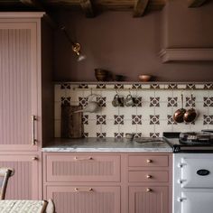 a kitchen with pink cabinets and white stove top in the center, along with pots and pans on the wall