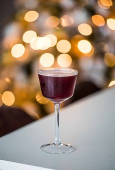 a glass filled with liquid sitting on top of a table next to a christmas tree