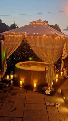 an outdoor hot tub lit up with candles and drapes on the patio at night