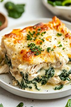 a white plate topped with lasagna covered in cheese and spinach leaves on top of a table