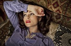 a woman sitting on top of a couch wearing a purple shirt and pearl necklaces