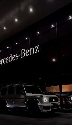 two cars are parked in front of a mercedes benz dealership at night with lights on