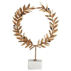 a gold leafy wreath on a white pedestal with a marble base and black beads