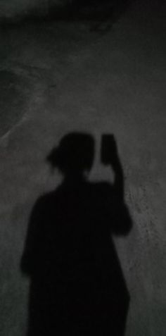 the shadow of a person holding a cell phone up to their head and wearing a hat