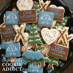 decorated cookies in the shape of camp woodin on a black plate with white writing