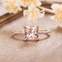 a pink diamond ring sitting on top of a wooden table next to white and yellow flowers