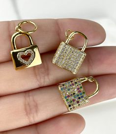 three different types of lock and key pendants on someone's hand, one with a heart