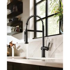 a kitchen sink with black faucet and white marble counter top in front of a window