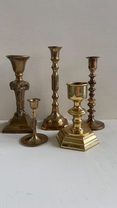 four brass candlesticks are lined up on a white surface and one is empty