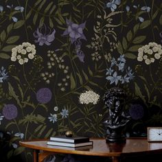 a wooden table topped with a clock next to a wallpaper covered in purple and white flowers