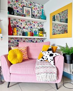 a pink couch sitting in front of a wall covered with pictures and other decor items