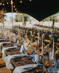 a long table set up with place settings for an outdoor wedding reception in the evening