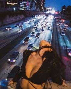 a woman is sitting on the edge of a bridge looking at traffic in the distance