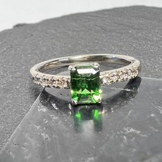 Emerald cut tsavorite garnet ring with diamond accented band set in 14k white gold. Beautiful emerald cut tsavorite garnet ring.  Garnet is precision cut with exceptional polish and symmetry, cut in house by Kreg. Emerald cut tsavorite garnet sourced from Kenya .71 carats 5.59mm x 4.23mm x 3.22mm SI Precision cut  8 - 1.7mm SI -GH natural diamonds .15 TCW currently US 5 1/2, for scale. Will size up or down 1 full size (select at checkout) I have 1 slightly larger (.8 carat) emerald cut tsavorite Emerald Cut Rings With Side Stones For Gift, Emerald Cut Jewelry With Side Stones For Anniversary, Classic Emerald Ring With Tsavorite Accent Stones, Square Cut Emerald Jewelry With Accent Stones, Emerald Cut Rings With Side Stones Fine Jewelry, Dazzling Emerald Cut Diamond Ring With Accent Stones, Baguette Cut Jewelry With Side Stones As Gift, Baguette Cut Jewelry With Side Stones For Gift, Gift Baguette Cut Jewelry With Side Stones