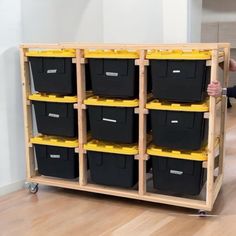 a man standing next to a wooden shelf filled with black and yellow bins on wheels