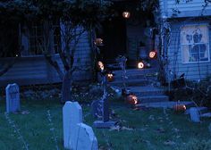 halloween decorations in front of a house with pumpkins on the ground and tombstones lit up at night