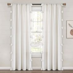 a white curtain with pom poms hanging on the side of it in front of a window