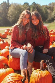 two young women sitting on pumpkins in a field