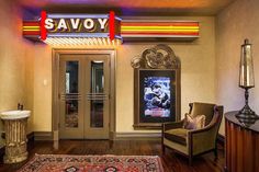 the entrance to savoy is lit up with red and yellow neon lights, while a chair sits in front of it