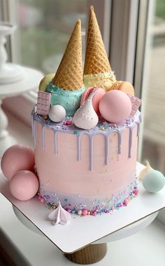 a pink cake with ice cream and candy on top sitting in front of a window