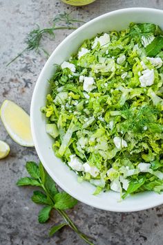 a white bowl filled with lettuce next to lemon wedges