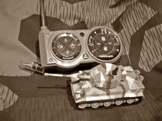 a toy tank with two dials sitting on top of a bed next to a pair of scissors