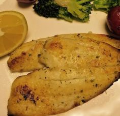 fish and vegetables on a white plate with lemons, broccoli and tomatoes