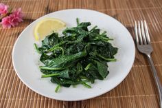 a white plate topped with spinach next to a fork and knife on top of a bamboo mat