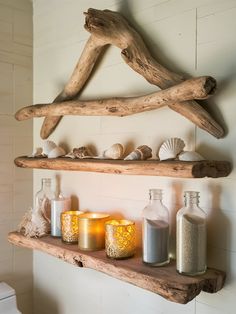 two shelves with candles and seashells are on the wall in front of a toilet