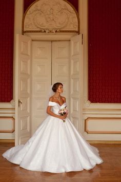 a woman in a white wedding dress standing next to an open door and holding a bouquet