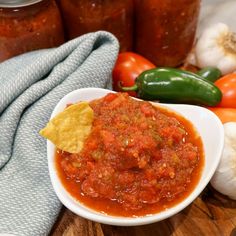 a white bowl filled with salsa on top of a wooden table next to peppers and garlic