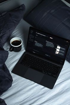 an open laptop computer sitting on top of a bed next to a cup of coffee