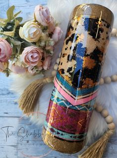 a gold and black travel mug next to some flowers on a white furnishing