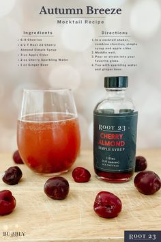 a bottle and glass filled with liquid sitting on top of a wooden table next to cherries