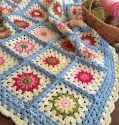 a crocheted blanket with flowers on it and a basket full of yarn next to it