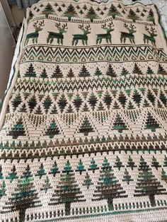 a crocheted blanket with deers and trees on it, sitting on a bed