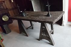 an old table with two candles on it in the middle of a room next to a fireplace