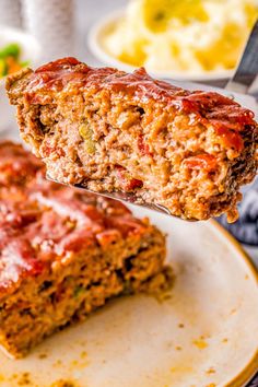 a piece of meatloaf on a plate being held by a fork with another slice in the background