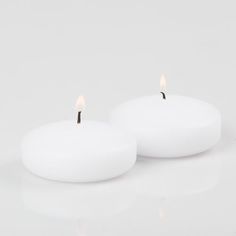 two white candles sitting side by side on a white surface with one candle lit and the other turned off