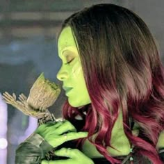 a woman with red hair and green makeup is holding a small bird in her hand