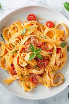 a white bowl filled with pasta, tomatoes and parsley on top of a marble table