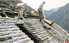 two men are working on the roof of a building that has been built into the side of a mountain