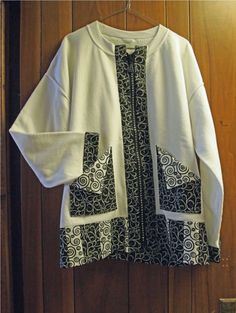 a white cardigan with black and white designs hanging on a wooden wall next to a door